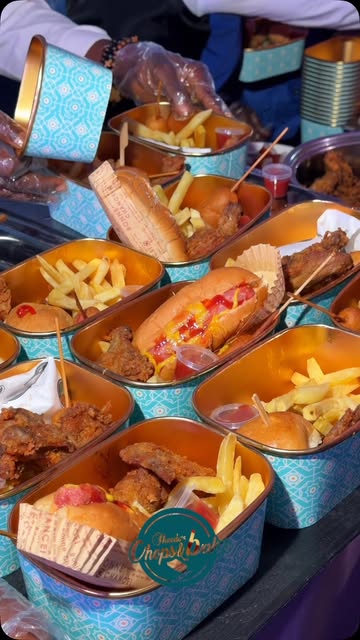 Rows of Chops & Bakes event boxes filled with fried chicken, sliders and fries, being handed out to guests at an event
